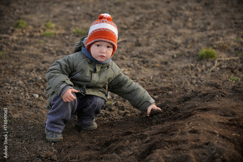 A young boy tries to help his parents plant potatoes in a vegetable garden in the village