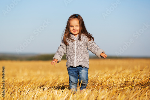 Happy 2 year old girl walking in a summer harvested field