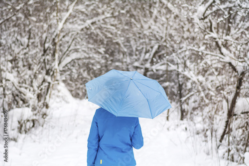 Girl with blue umbrella walking in the winter park