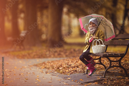 Happy young girl holding umbrella and sitting at the bench. Autumn theme. photo