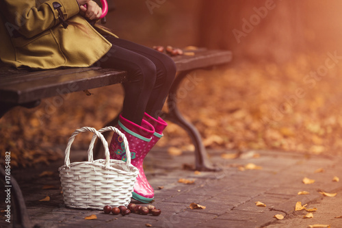 Young girl holding umbrella and sitting at the bench. Autumn theme. Basket on the ground. photo