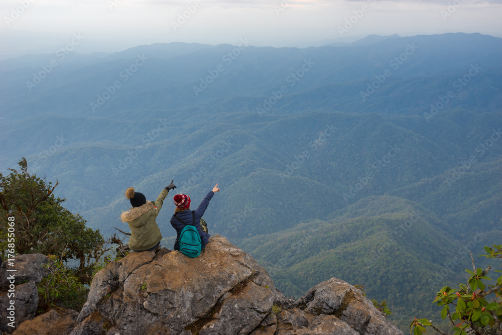 Two tourists are watching the beautiful scenery on the top of the hill in the morning.