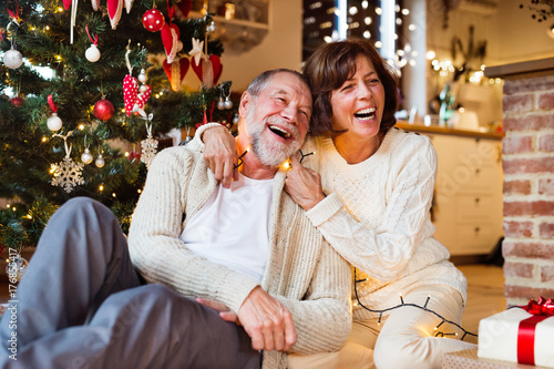 Canvastavla Senior couple in front of Christmas tree with presents.