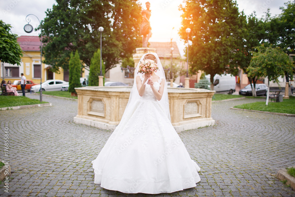 the bride in an elegant white dress stands near a monument in the city center the bride in an elegant white dress stands near a monument in the city center