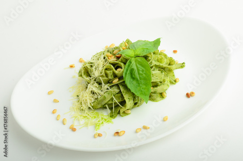 Pesto pasta with cheese and pine nuts decorated basil on a plate isolated on white background