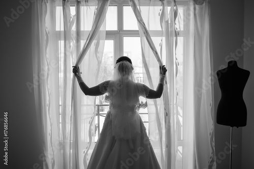 elegant bride in a white dress standing near the window and waiting for her lover