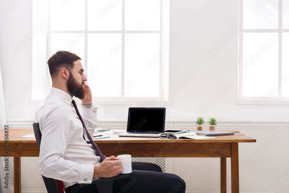 Serious businessman talking on cell phone with laptop in modern office Serious businessman talking on cell phone with laptop in modern office
