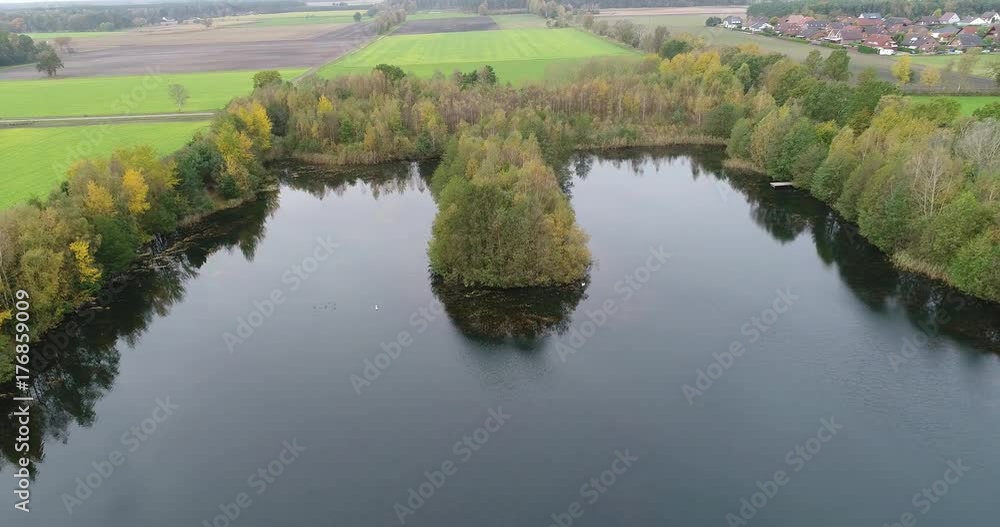 Aerial photograph, flight with the drone above an island densely covered with trees in a pond with some swans. Aerial photograph, flight with the drone above an island densely covered with trees in a pond with some swans.