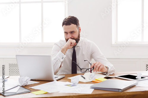 Young serious businessman with laptop in modern white office