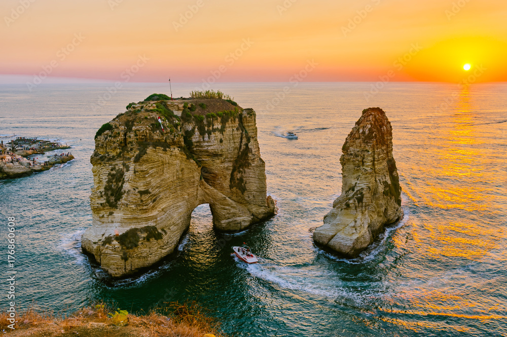 Obraz premium Piękny zachód słońca na Raouche, Pigeons 'Rock. W Bejrucie w Libanie Słońce i kamienie odbijają się w wodzie, gęste chmury na niebie.