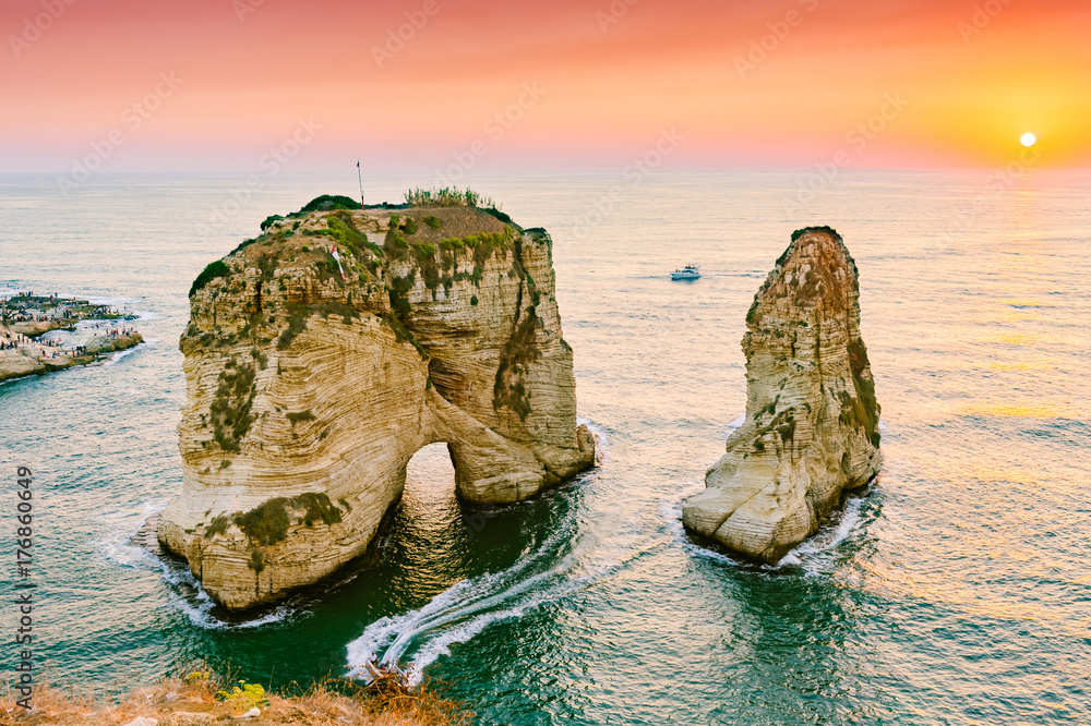 Fototapeta premium Piękny zachód słońca na Raouche, Pigeons 'Rock. W Bejrucie w Libanie Słońce i kamienie odbijają się w wodzie, gęste chmury na niebie.
