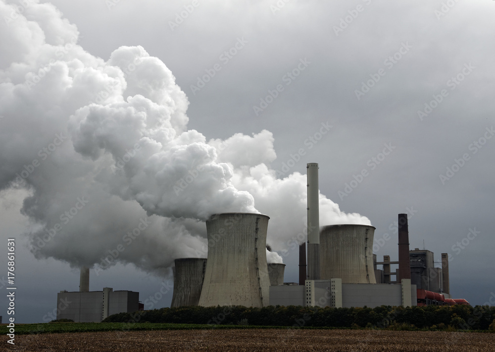 Elektrizitätswerk mit Emissionen, düsteren Wolken und Feldern
