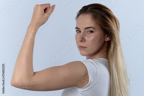 attractive confident young woman shows biceps. Portrait on a white background, expressive look at the camera