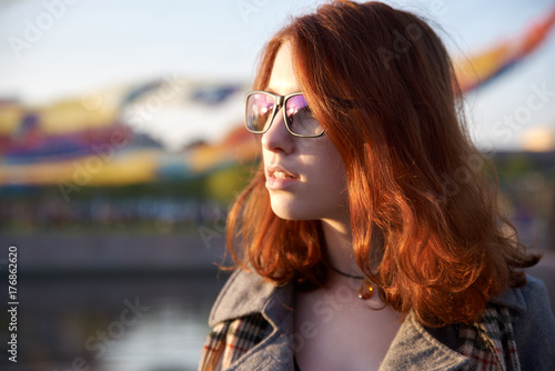 Beautiful young woman with red hair in the park. Sunlight. Portrait of a smiling red-haired girl in a park in the last rays. Very beautiful portrait of a redheaded girl in a park at sunset