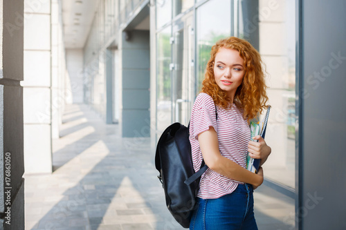 Young redhead student girl with a backpack and notepads