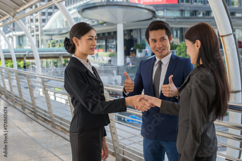business man show thumb up and two business woman shaking hands for demonstrating their agreement to sign agreement or contract between their firms, companies, enterprises. success concept