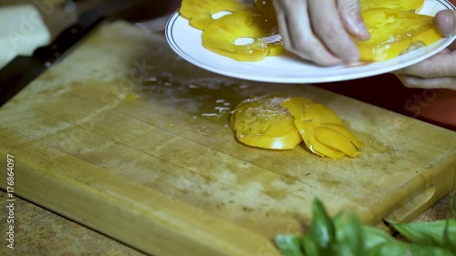 A cook arranges yellow heirloom tomato slices onto a white china plate. photo