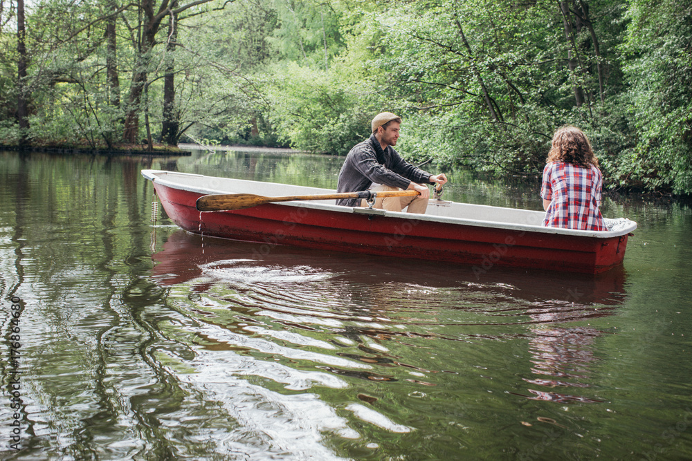 Young Caucasian Man Rowing Small Boat on Lake with Girlfriend Young Caucasian Man Rowing Small Boat on Lake with Girlfriend