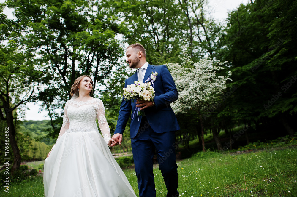 Stunning wedding couple enjoying each other's company in park with blossoming trees on the background. Stunning wedding couple enjoying each other's company in park with blossoming trees on the background.