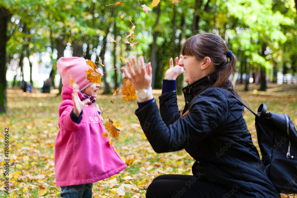 Fototapeta premium happy family mother and girl child little daughter play cuddling on autumn walk in nature outdoors in the park with fall leaves