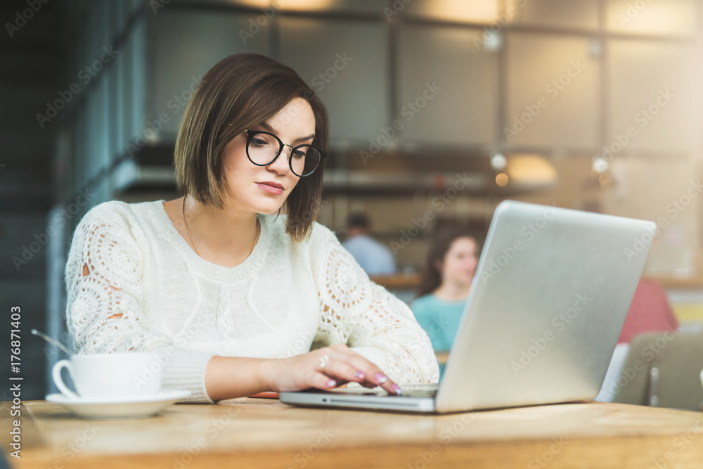 Young businesswoman in glasses sitting in cafe at table and working on laptop. Student is studying online. Hipster girl using computer. Online education, marketing, e-learning. Social media, network. Young businesswoman in glasses sitting in cafe at table and working on laptop. Student is studying online. Hipster girl using computer. Online education, marketing, e-learning. Social media, network.