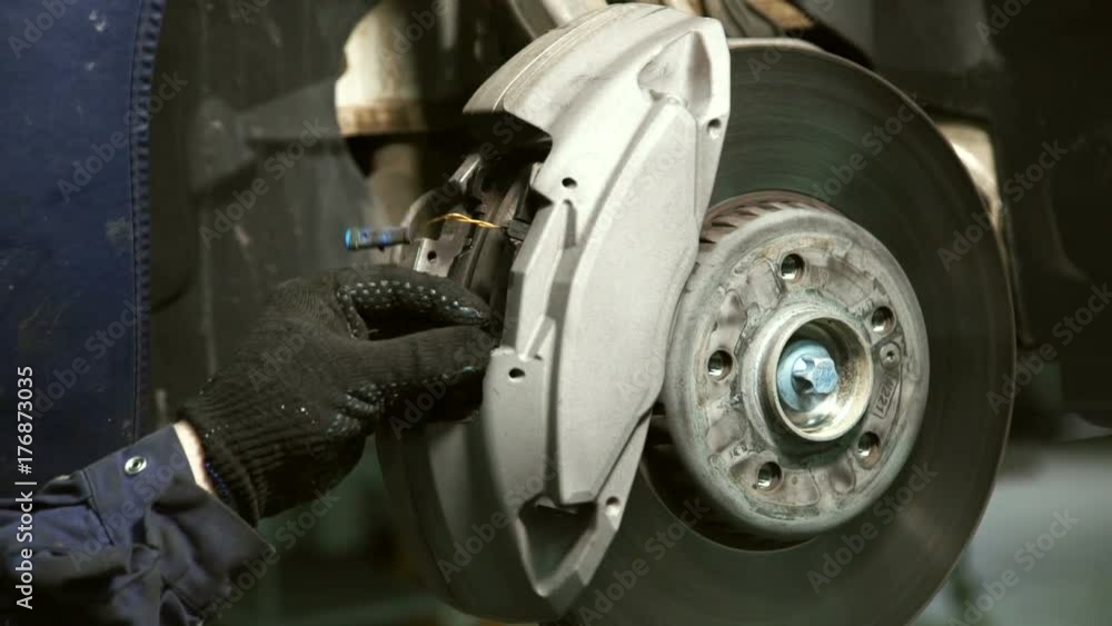 Hand gloves makes replacing brake pads on wheel. Mechanic inserts item into spinning mechanism of vehicle during servicing and repair. Hand gloves makes replacing brake pads on wheel. Mechanic inserts item into spinning mechanism of vehicle during servicing and repair.
