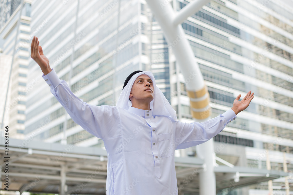 Muslim man praying in public place and modern building background Muslim man praying in public place and modern building background