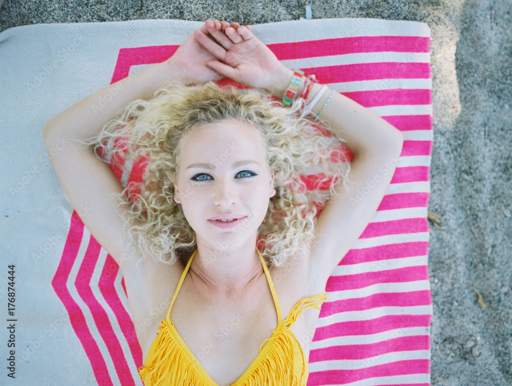 blonde curly haired girl on pink graphic rug on beach in yellow bikini  Stock Photo | Adobe Stock