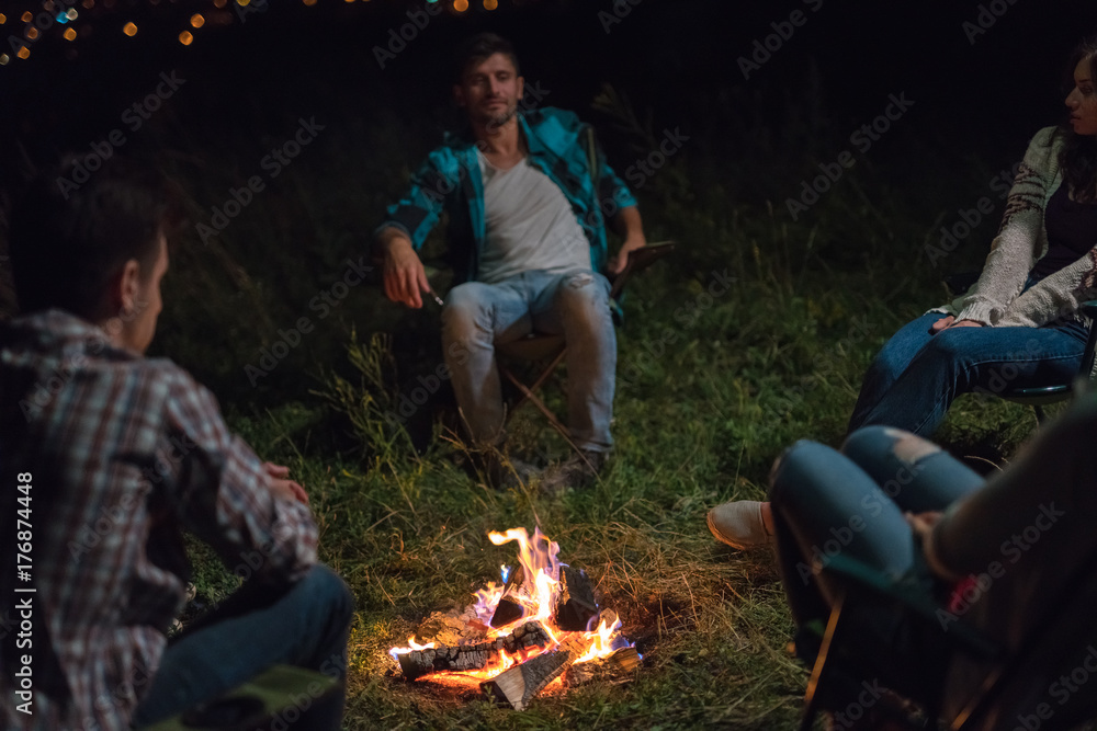 The young people sit near the bonfire. evening night time The young people sit near the bonfire. evening night time