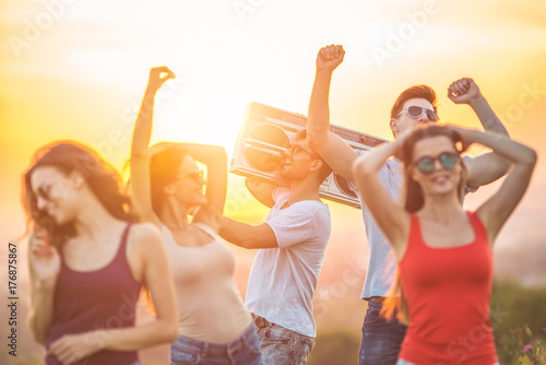 The happy friends dancing with a boom box on the sunny background
