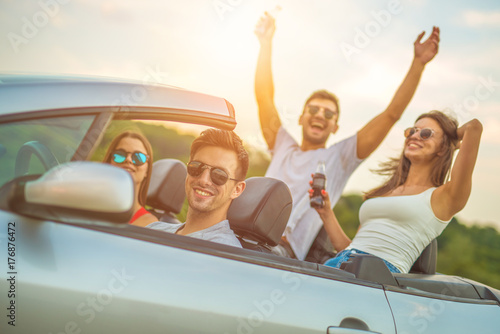 The happy friends sit in a cabrio on the sunny background