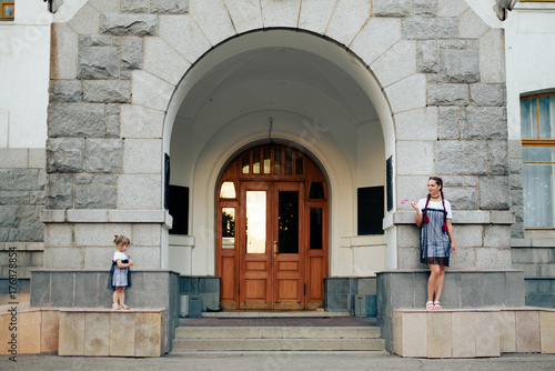 little girl with her mother in the identical dresses with candy on a background of gray buildings and arches