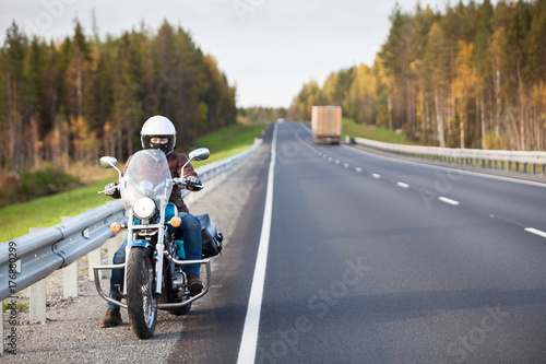Woman on a motorcycle resting on the roadside of a country highway with empty road