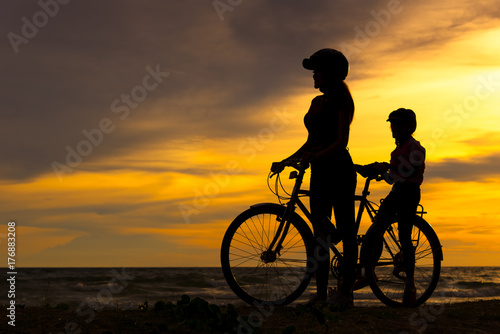 Silhouette biker lovely family at sunset over the ocean. Mom and daughter bicycling at the beach. Lifestyle Concept.