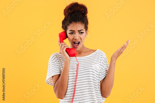 Angry african woman screaming while talking on red telephone