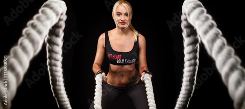 Battle ropes session. Attractive young fit and toned sportswoman working out in functional training gym doing crossfit exercise with battle ropes. Fitness and workout motivation photo