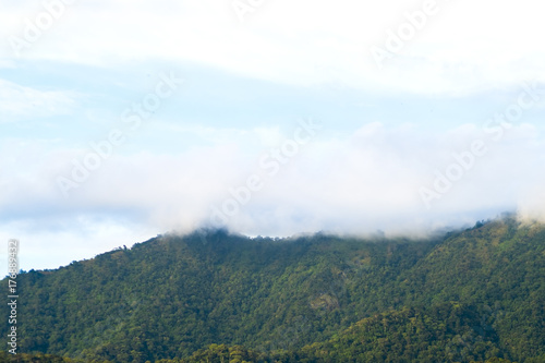 View from below  Looking to beautiful green mountain covered with white mist on the top and yellow light with blue sky and some clouds  After the rain at sunset. North of Thailand.