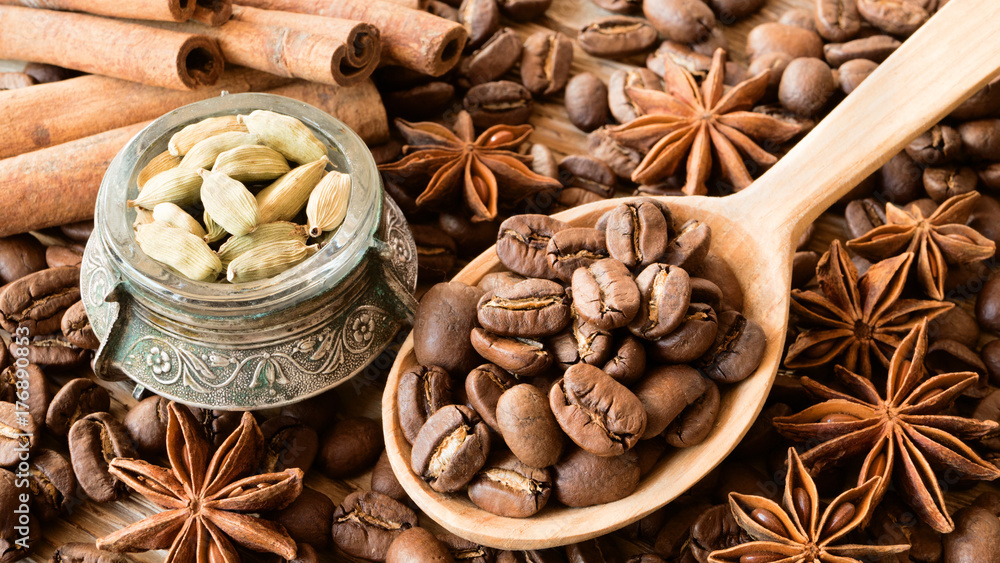 Roasted coffee beans in wooden spoon with anise stars, cinnamon sticks and cardamom in small bowl Roasted coffee beans in wooden spoon with anise stars, cinnamon sticks and cardamom in small bowl