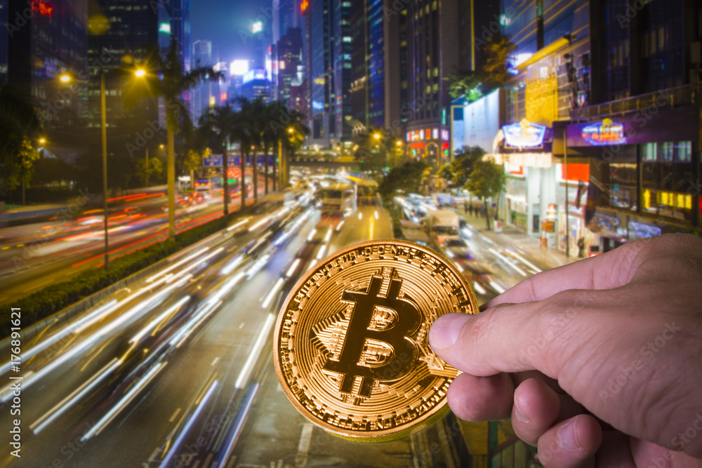 Fototapeta premium Hand holding a bitcoin with night view of Hong Kong in the background.