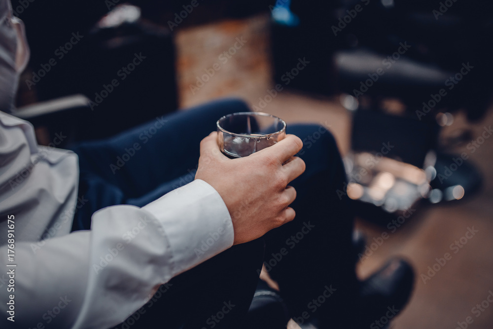 man is holding a glass of whiskey in the barber's chair in barbershop