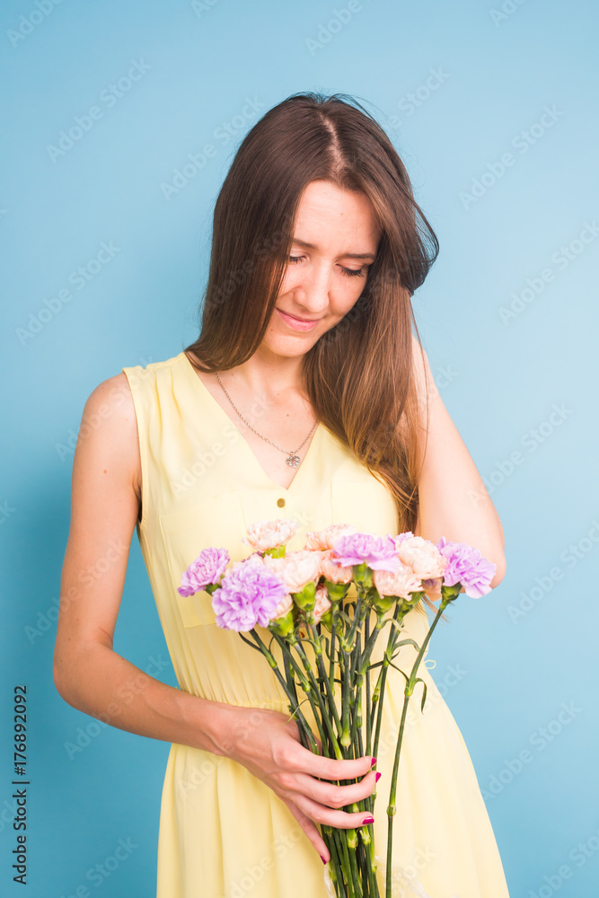 Smiling pretty young woman holding bouquet of flowers over blue background. Smiling pretty young woman holding bouquet of flowers over blue background.