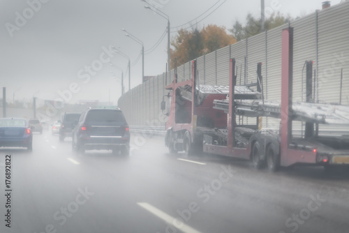 Cars and a truck for passenger cars are speeding on a wet road. highway junction at the middle of the day. clouds and rain.