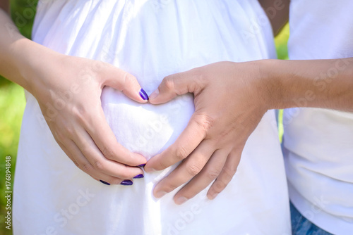 Pregnant couple showing a heart with your hands near the round tummy