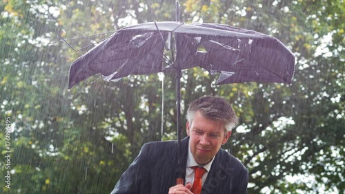 Businessman sheltering underneath a broken umbrella in the rain