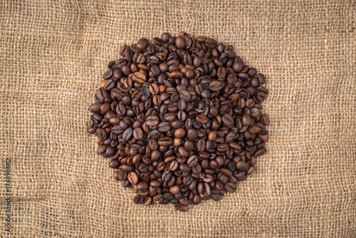 Pile of coffee beans in the middle on jute background.