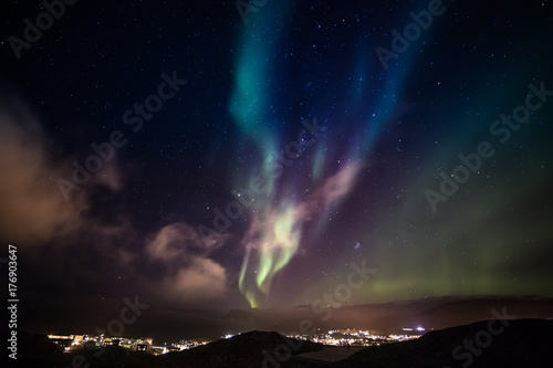 Aurora Borealis with shining stars on the sky over the mountains and highlighted city  Nuuk  Greenland