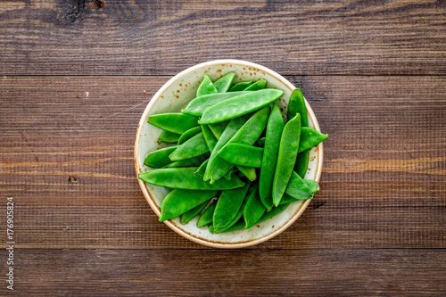 Fresh pea pods on the plate on dark wooden background top view copyspace