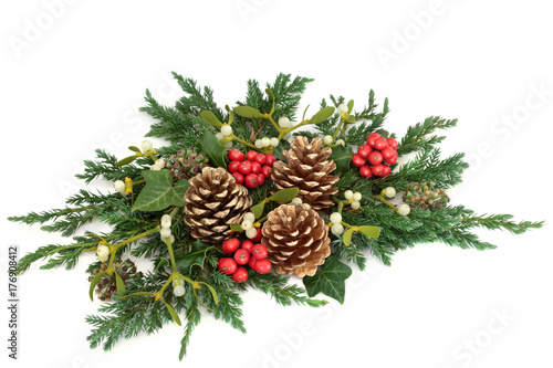Christmas floral table decoration with holly, gold pine cones, ivy, mistletoe, cedar and juniper leaf sprigs on white background.
