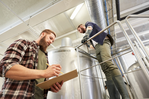 men with clipboard at brewery or beer plant kettle
