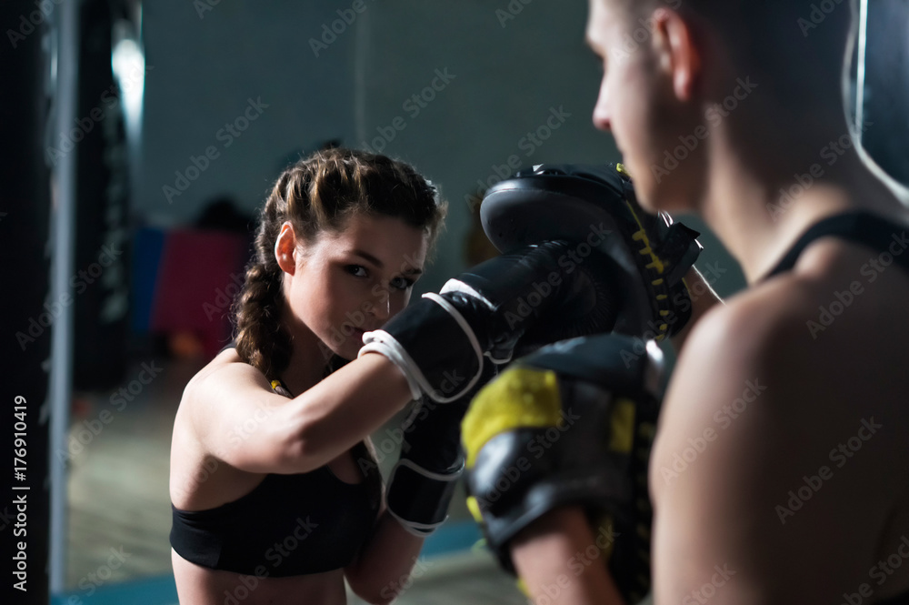 Young fighter boxer fit girl wearing boxing gloves in training with personal trainerin gym. Low key selective focus image. Woman power Young fighter boxer fit girl wearing boxing gloves in training with personal trainerin gym. Low key selective focus image. Woman power